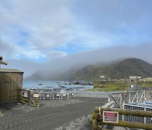 A helicopter with a sling load of cargo dangling beneath it, hovers above the shoreline at Macquarie Island.