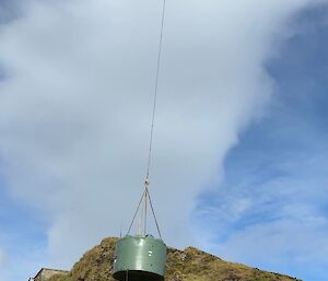 A helicopter slingloading a round, green water tank into place beside another tank.