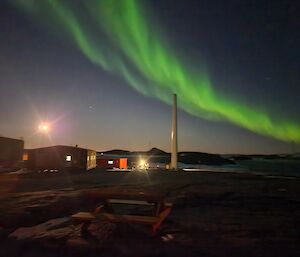 photo of station buildings with aurora overhead and a full moon partially lighting up the night sky
