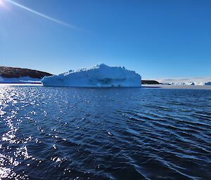 picture of a floating berg in the water, with a rocky coastline in the background