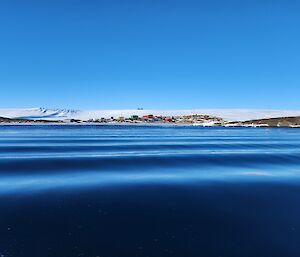 A photo taken in a boat, almost at water level, of the water in foreground and station buildings and terrain in far background