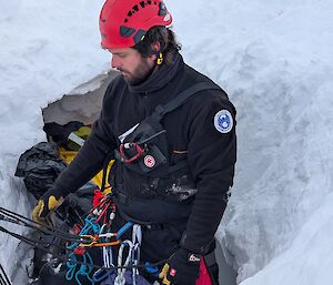A man with rescue gear and a red helmet in a deep hole in the ice