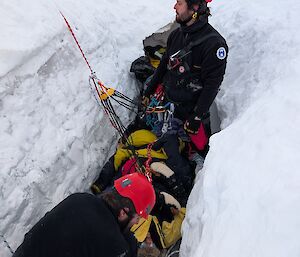 Two people in red helmets with ropes in a deep hole in the ice
