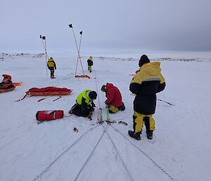Five people organising ropes on an open snowy plain