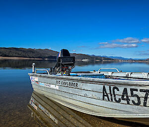 An aluminium boat sith on a still lake with a bright blue sky in the background