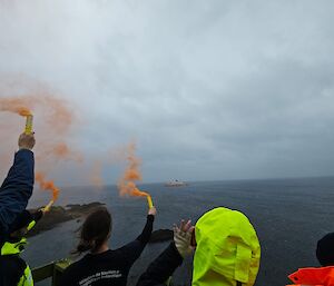 A red ship in the distance and the backs of people letting off flares
