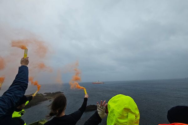 A red ship in the distance and the backs of people letting off flares