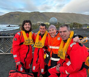 Four people in red helicopter immersion suits with Macquarie Island behind them