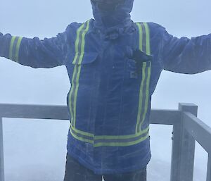 An expeditioner standing on the Red Shed balcony, buffeted by blizzard winds and low 'white-out' conditions.