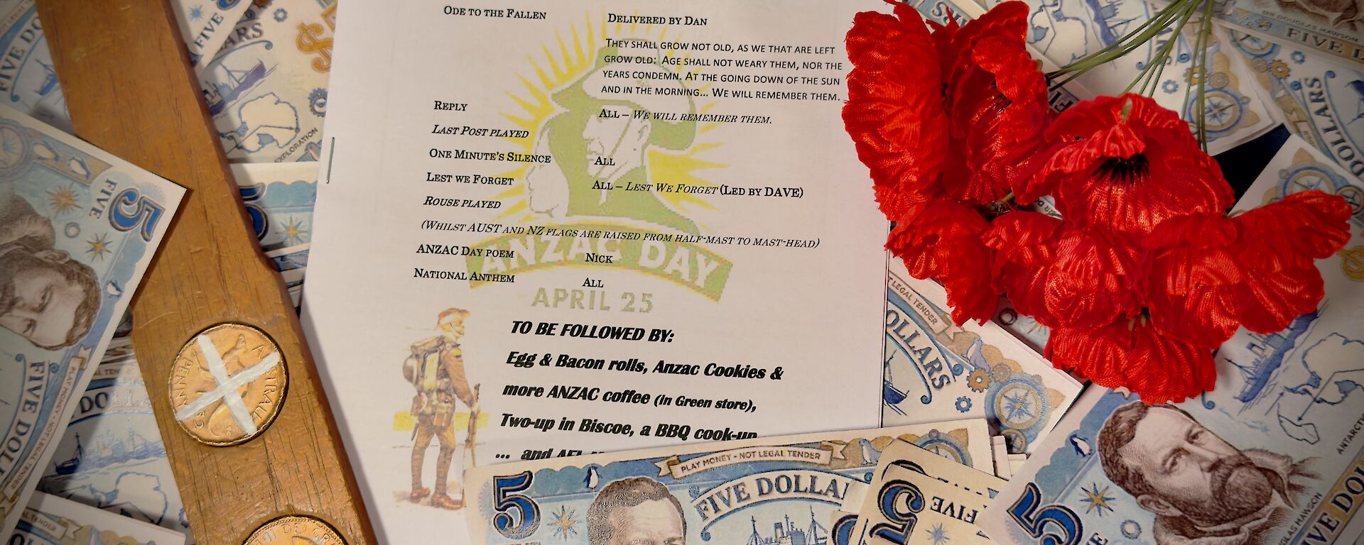 A photo of Mawson's ANZAC Day service program, surrounded by poppies, two-up paddle with coins and fake Mawson money.
