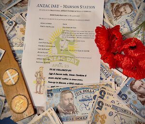 A photo of Mawson's ANZAC Day service program, surrounded by poppies, two-up paddle with coins and fake Mawson money.