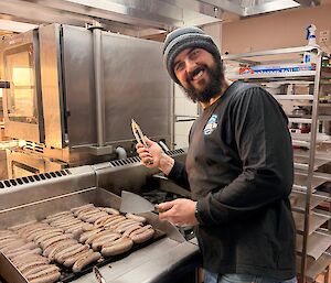 Expeditioner in the kitchen cooking sausages for the ANZAC Day 'sangas'.