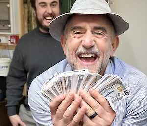 An expeditioner smiling while holding a significant wad of Mawson Bucks cash.