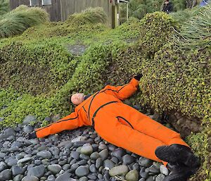 An orange-wearing dummy lying on a rocky beach with grassy slopes behind it