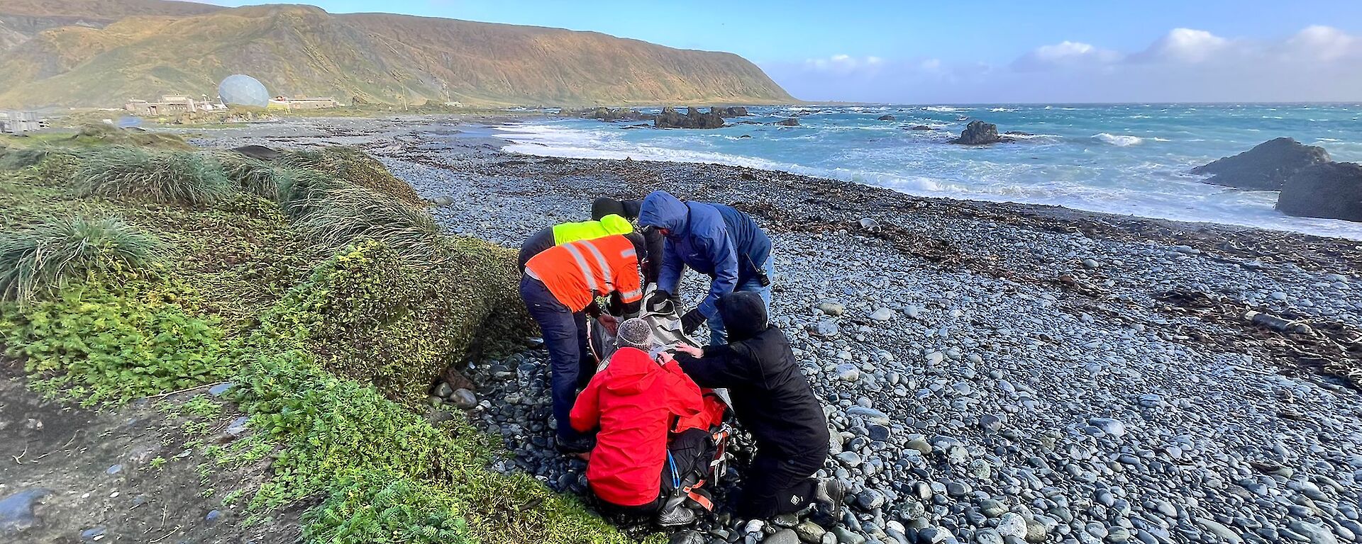 People standing around the orange dummy on a rocky beach