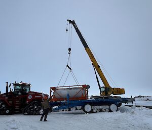 A fuel tank being lifted by crane onto a tractor towed trailer