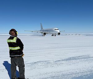 a staff member watches a large passenger plane taxiing on the ice runway