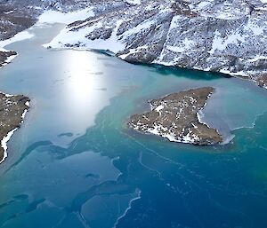 picture taken from a plane, looking over rocky outcrops and a body of bluish-green water with an island in the middle