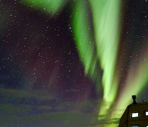 a green aurora overhead with stars and clouds visible, with a building in the foreground
