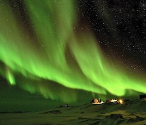 an amazing green aurora dominating the sky over a station, with stars visible in the backdrop