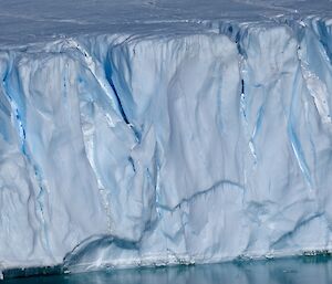 An ice shelf over the water, with massive crevassing and deep slots carved into the wall