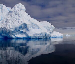 An iceberg of differing blue and white colours in calm water, with its reflection captured in the deep blue water.