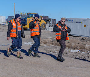 three expeditioners in high visibility vests walking on station, with some making gestures to the camera