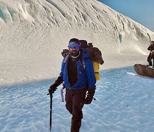 Expeditioner dressed in warm gear with ice axe in hand, walking on blue sea ice with ice wall in background