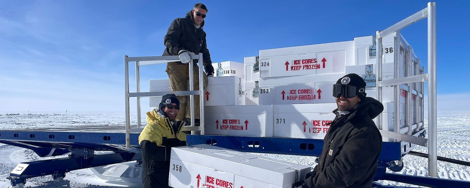 Three men lift metre-long boxes of ice cores on to a sled.