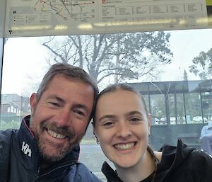 A bearded man in a blue jacket poses with a younger woman with plaited hair wearing a black jacket.
