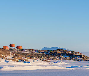 Picture taken on sea ice of a rocky outcrop of Bechervaise Island, with three orange huts on top