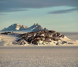 picture taken from the sea ice, looking at jagged mountain ranges and coastal rock formations along the coastline