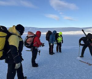 expeditioners standing on the sea ice while one person drills into the ice to test the depth