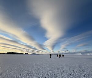 distant expos walking on the sea ice, with amazing cloud trails and patterns overhead