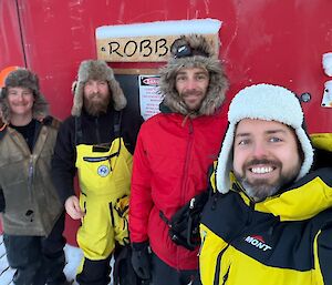 A group of smiling people with a red hut behind them