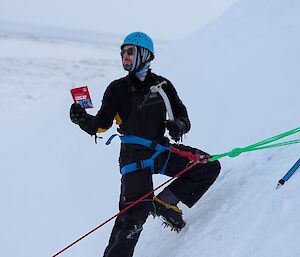 A person climbing an ice cliff reading a First Aid manual