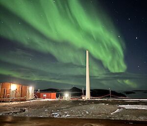 Picture of a green aurora overhead of station buildings, accompanied by stars