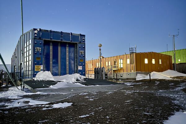 A blue building with large front doors, alongside the station's yellow operations building