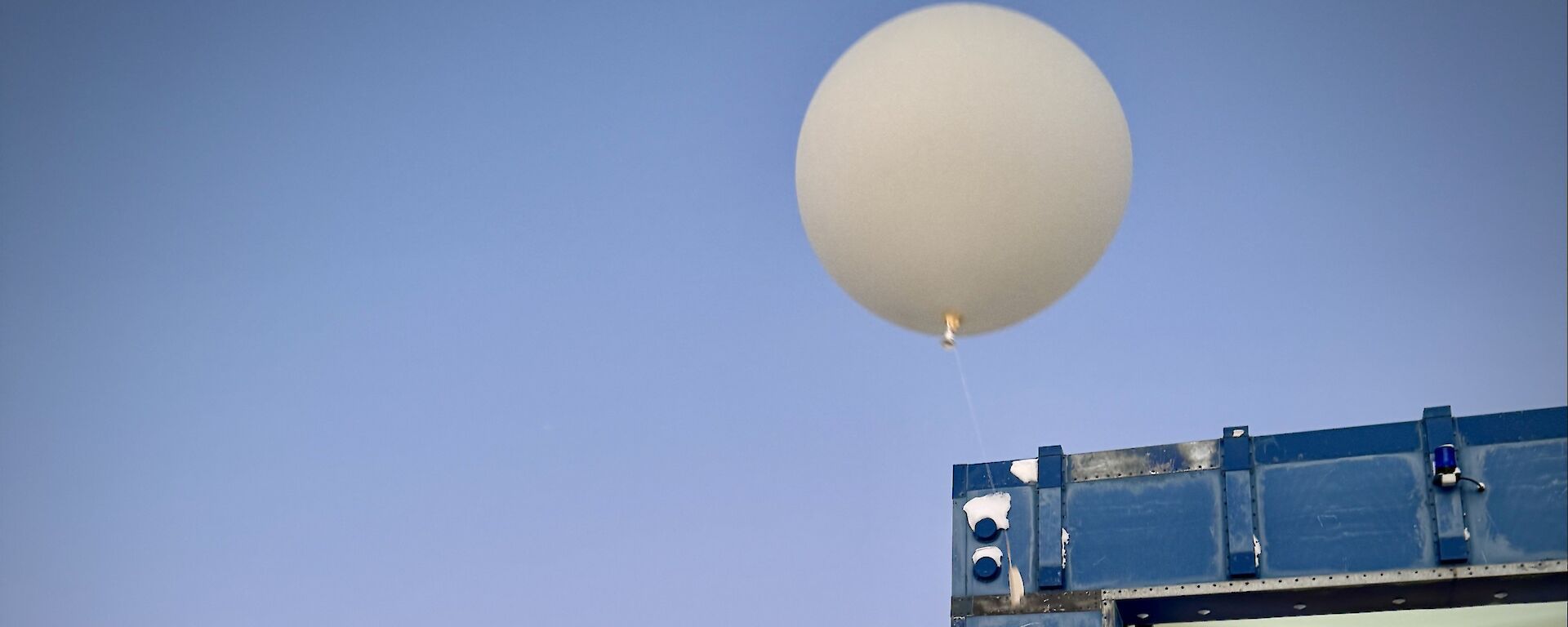 A Bureau of Meteorology observer dressed in job-specific overalls and balaclava, releasing a balloon into the sky