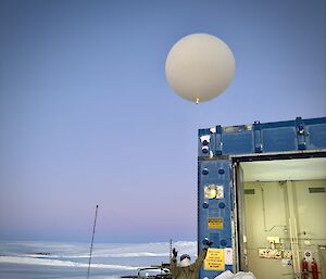 A Bureau of Meteorology observer dressed in job-specific overalls and balaclava, releasing a balloon into the sky