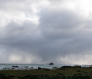 Grey rainclouds on the horizon with ocean and land in the foreground