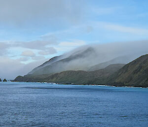 Fog trails down a mountain slope towards the ocean.