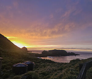 A purple and orange sunset over the beach, with station infrastructure visible in the foreground.