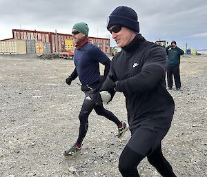 two men wearing thermal layers are starting to jog on a run, one is setting the timer on his watch.