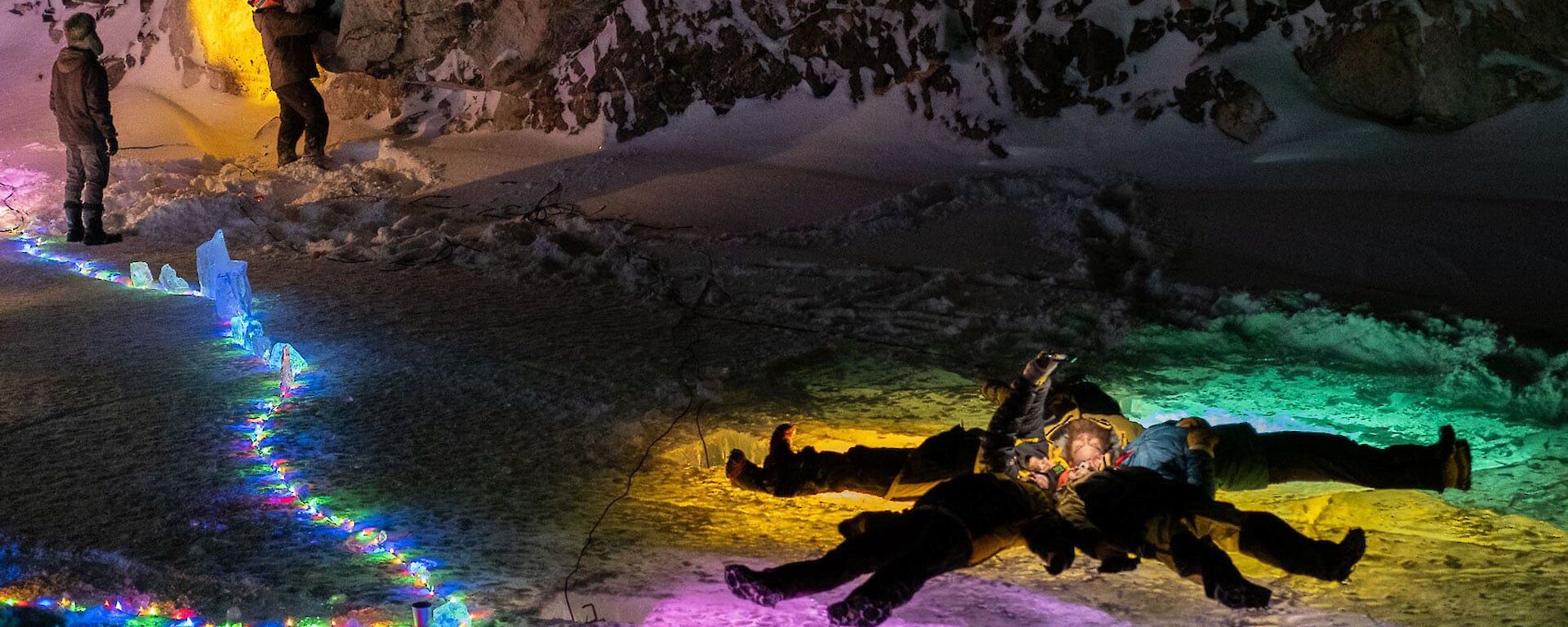 A group of expeditioners on the ice at night, surrounded by coloured lights