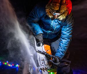 An expeditioner using a chainsaw to cut through the ice