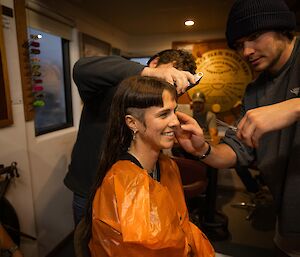 A woman with half her hair cut and two hairdressers finessing her style.