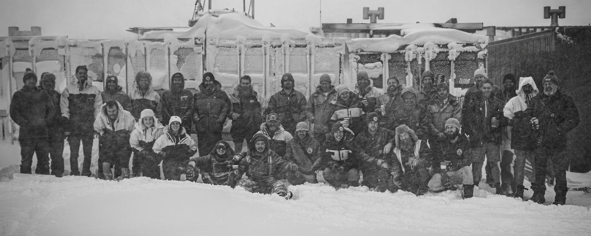 Black and white photo of a group out in the snow with sheds behind them