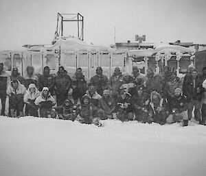 Black and white photo of a group out in the snow with sheds behind them