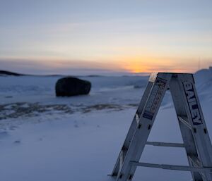 A ladder surrounded by snow, overlooking the sea ice and fading sunlight in the background